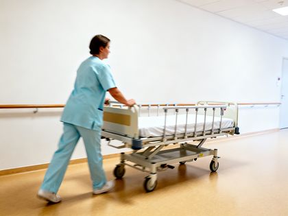 Pflegekraft schiebt ein Bett durch den hellen Flur einer Klinik